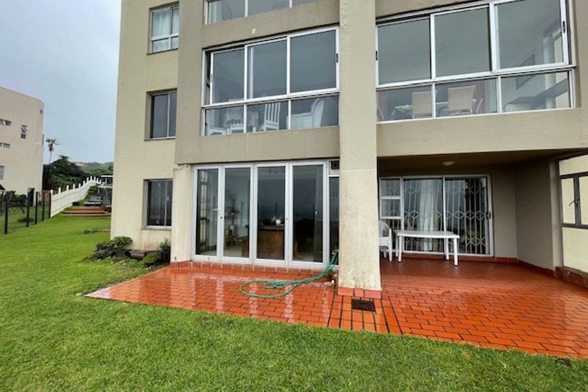 Rear view of the apartment building featuring a terracotta tiled patio, large aluminium sliding doors, and expansive windows overlooking the communal garden area.