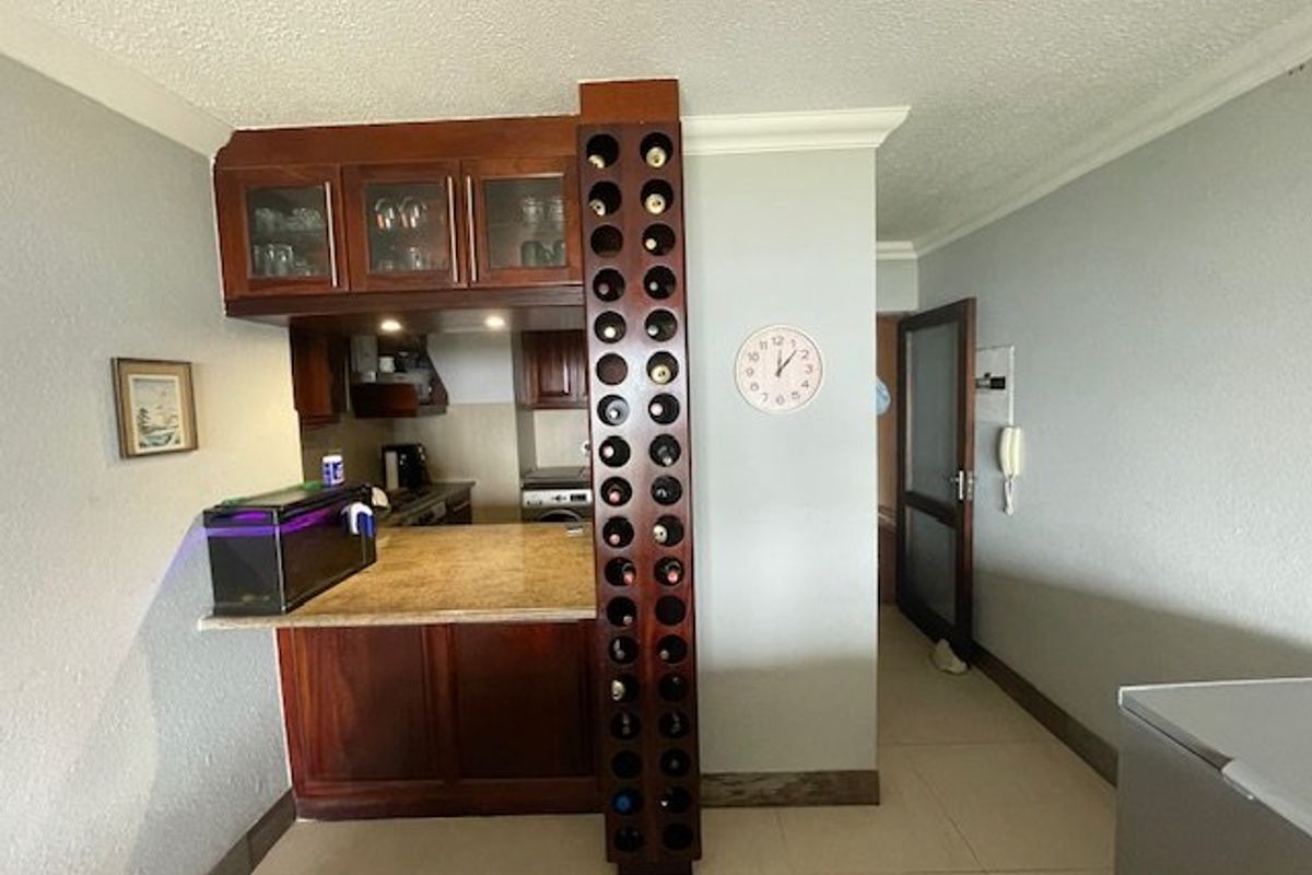 Compact kitchen area featuring wooden cabinetry, a built-in wine rack, and granite countertops, opening into a tiled hallway.