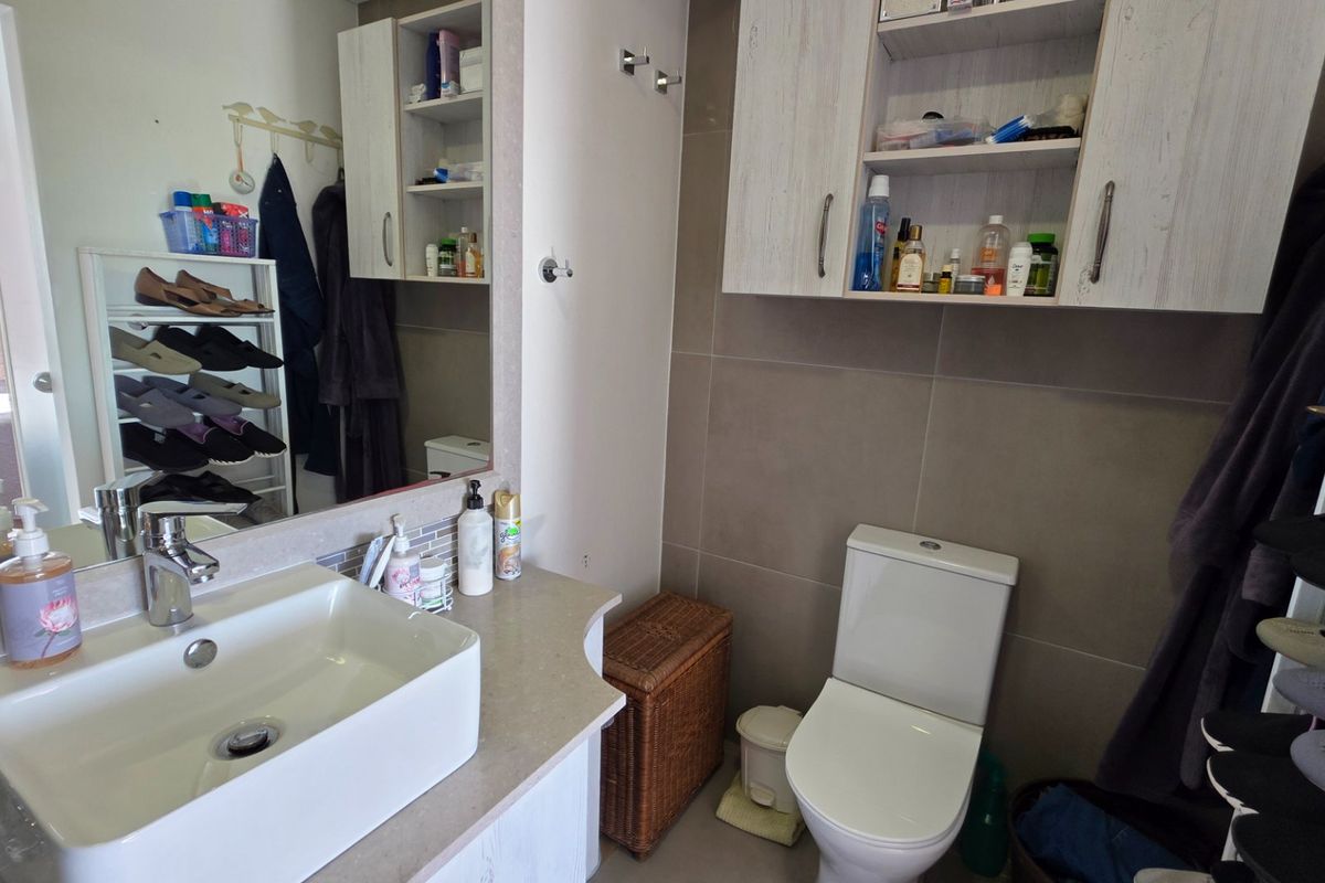 A functional bathroom featuring a modern vessel sink, vanity storage, wall-mounted cabinets, and neutral wall tiling.
