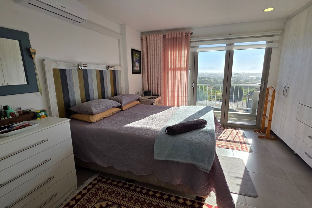A well-maintained bedroom featuring built-in wardrobes, tiled flooring, a split-system air conditioner, and direct access to a balcony with scenic views.