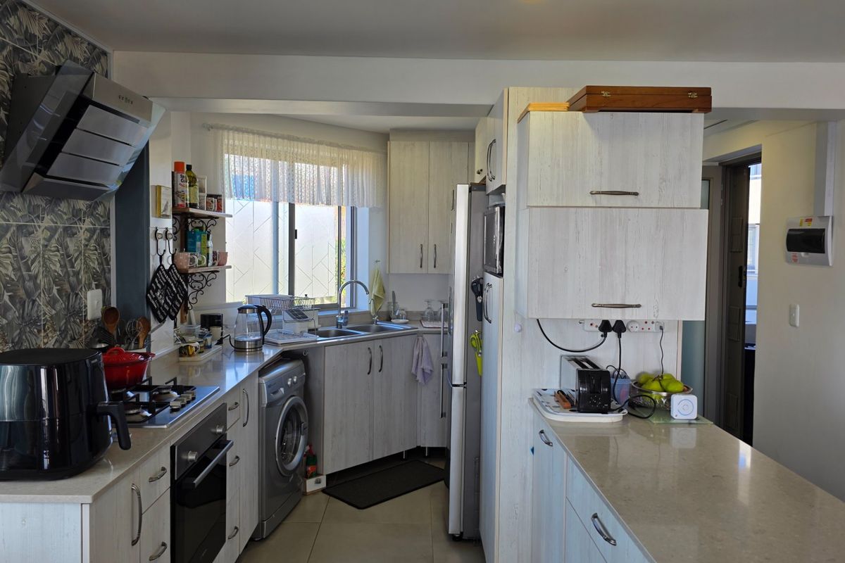 A functional kitchen featuring light wood-grain cabinetry, stone countertops, a built-in oven, gas hob, and integrated laundry facilities.