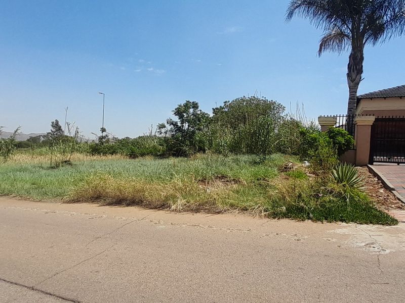 A vacant residential plot featuring a paved driveway and perimeter fencing, situated adjacent to an existing property.