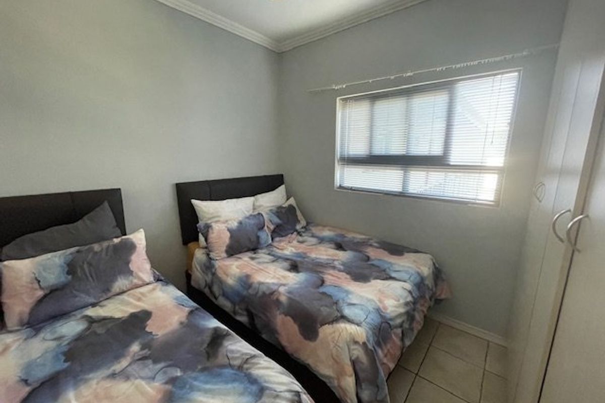 A functional bedroom featuring tiled flooring, built-in cupboards, a ceiling fan, and a window with venetian blinds.
