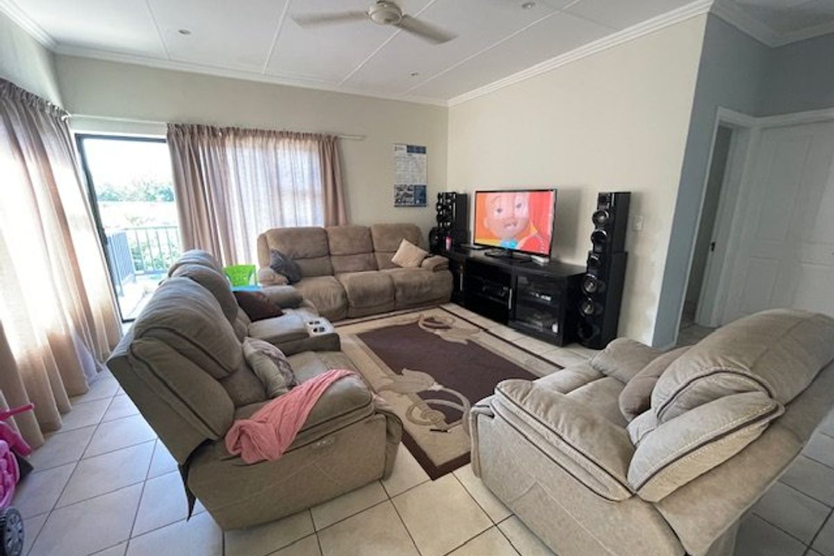 A spacious living room featuring tiled flooring, a ceiling fan, and a sliding glass door providing access to an outdoor balcony area.
