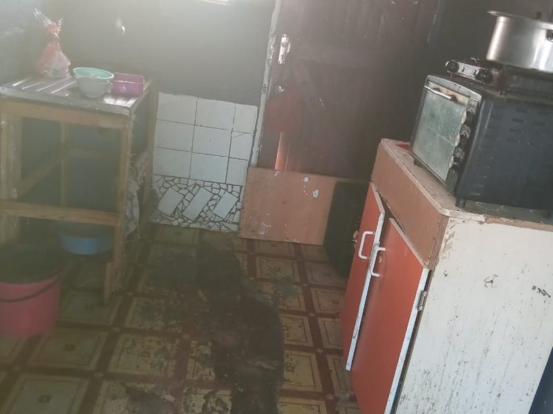 A small kitchen area featuring basic cabinetry and tiled splashback, currently showing significant wear and requiring maintenance or renovation.
