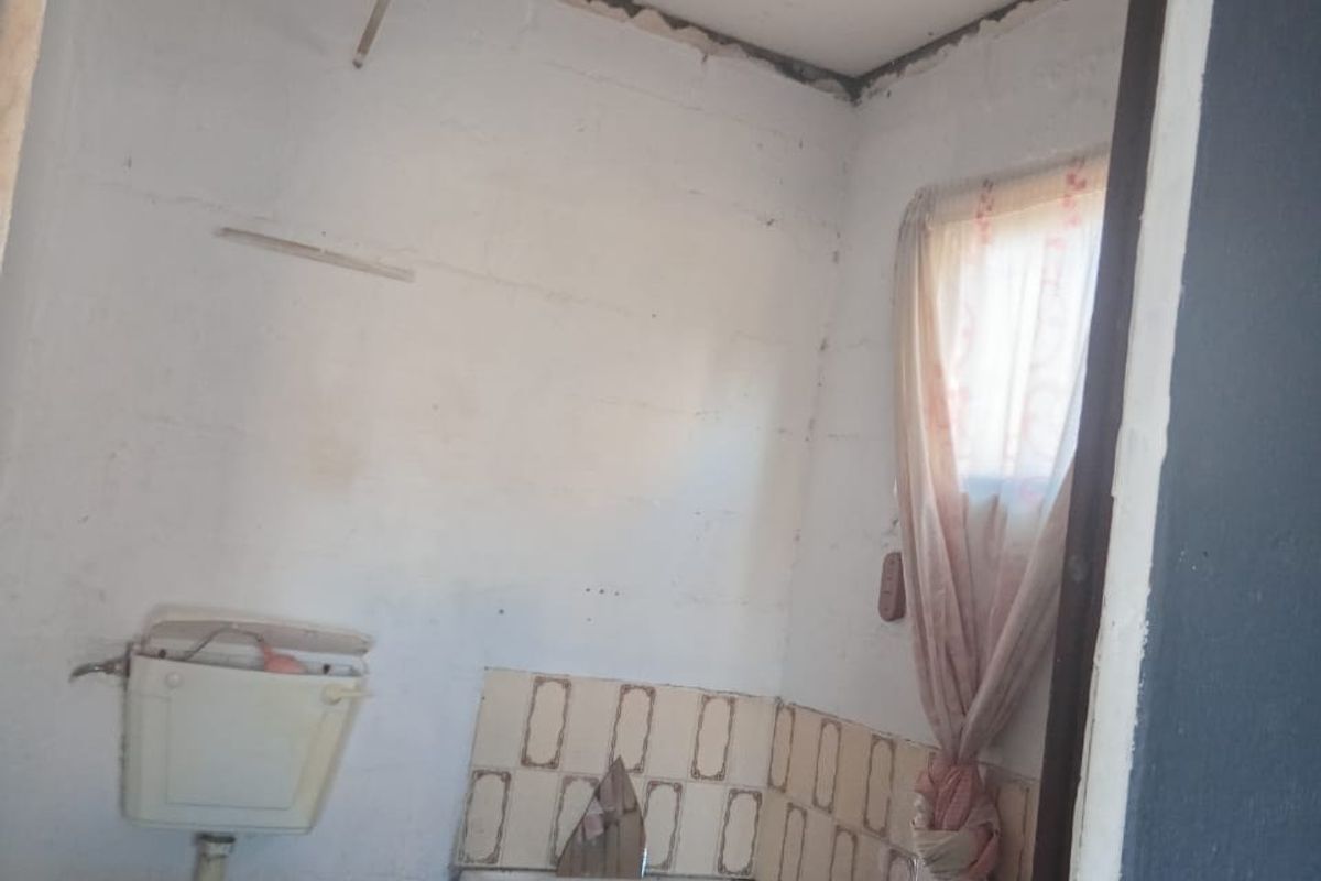 A small, dated bathroom requiring significant renovation, featuring a basic toilet, bathtub, and tiled splashback with visible wear and ceiling damage.