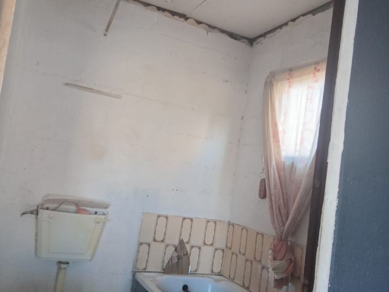 A small, dated bathroom requiring significant renovation, featuring a basic toilet, bathtub, and tiled splashback with visible wear and ceiling damage.