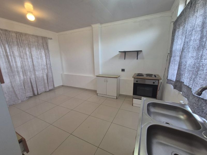 A functional, empty kitchen space featuring tiled flooring, a built-in oven with electric hob, and a double stainless steel sink.