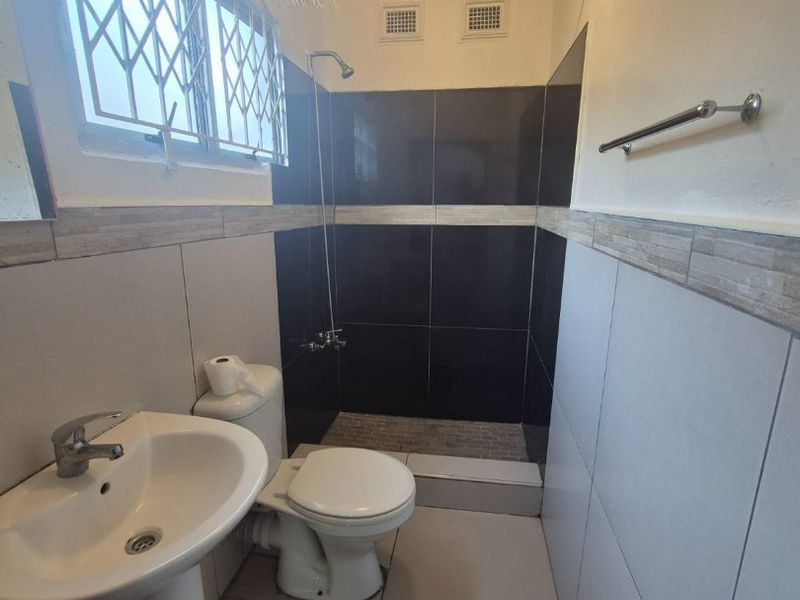 A functional bathroom featuring a pedestal basin, toilet, and a walk-in shower with dark tiled accents and neutral wall tiling.