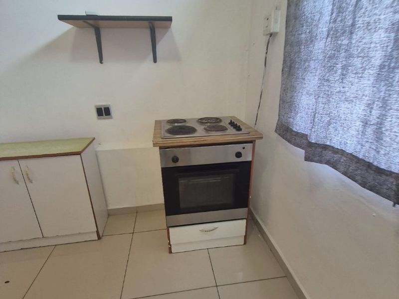 A compact kitchen area featuring a built-in oven, electric hob, base cabinetry, and tiled flooring, requiring some cosmetic updates and electrical tidying.