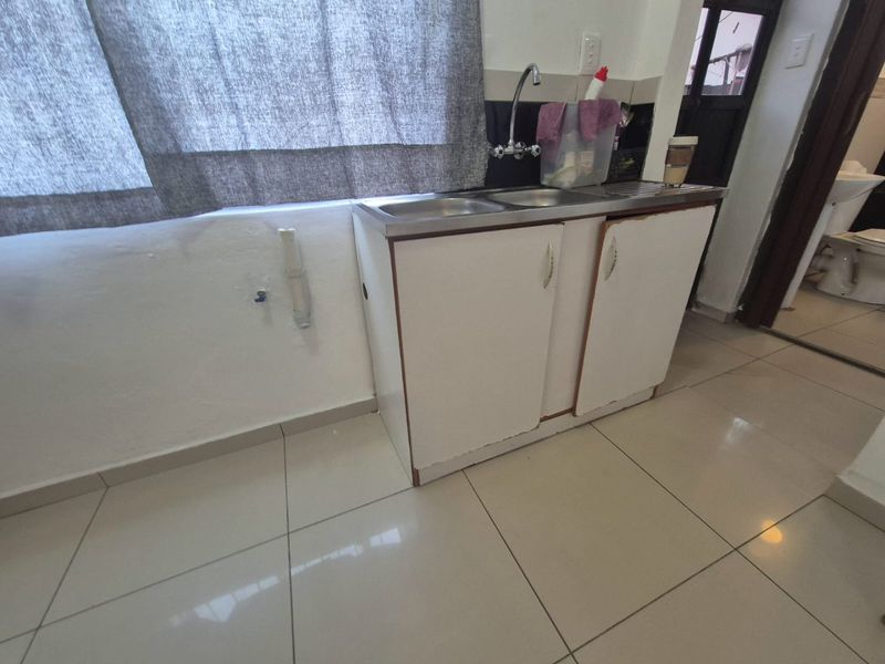A functional scullery or utility area featuring a stainless steel sink, built-in base cabinetry, and tiled flooring.
