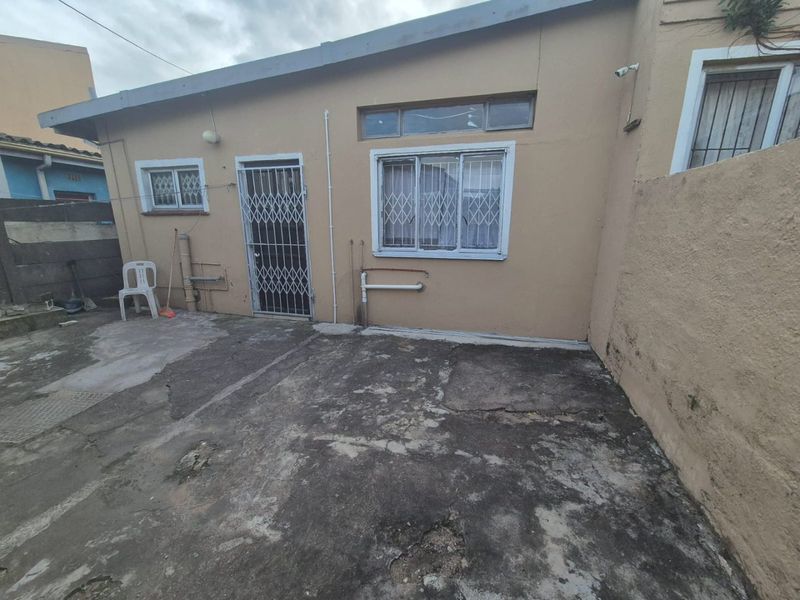 Rear exterior view of the property featuring a concrete paved area, security gates, and security bars on the windows.