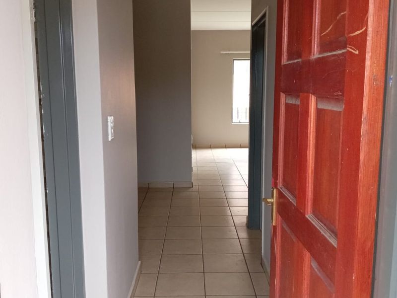 A vacant hallway featuring neutral wall paint and tiled flooring, leading towards an open living area with natural light.