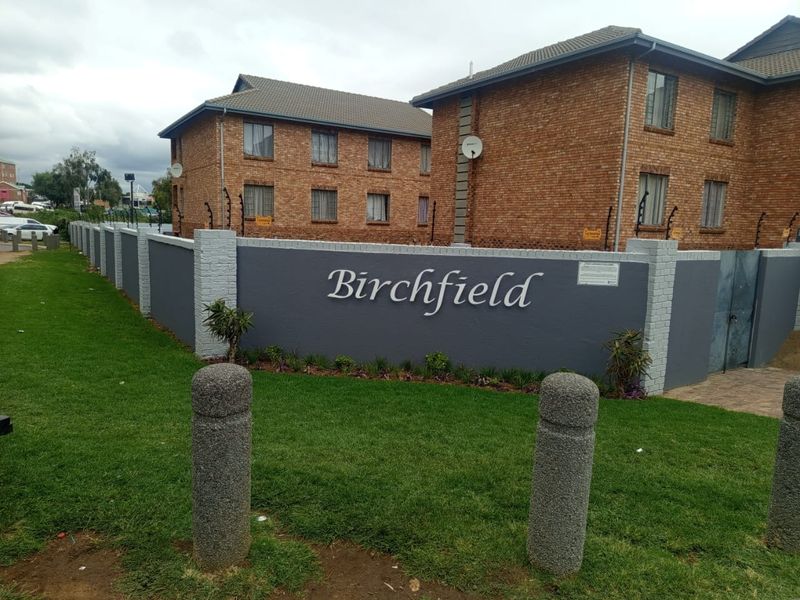 Exterior view of the Birchfield apartment complex, featuring face brick buildings, a secure perimeter wall with electric fencing, and a well-maintained lawn.