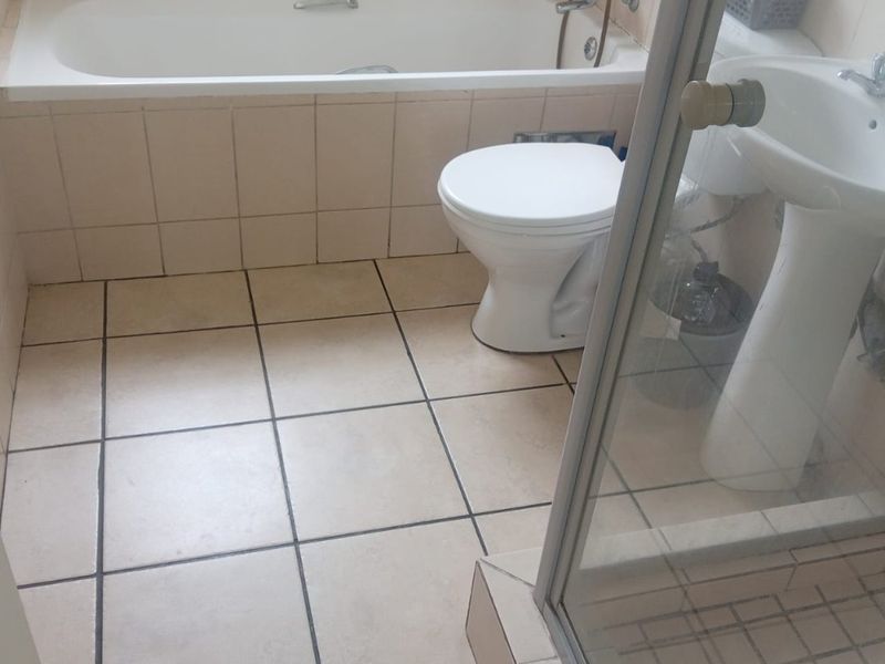 A functional bathroom featuring a bathtub, pedestal basin, toilet, and a separate shower enclosure with neutral ceramic tiling throughout.