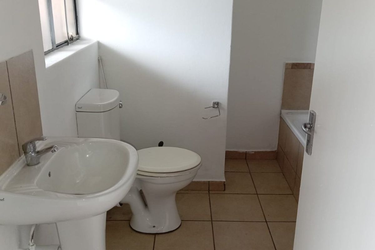 A functional bathroom featuring a pedestal basin, toilet, and bathtub with neutral tiled flooring and splashbacks.