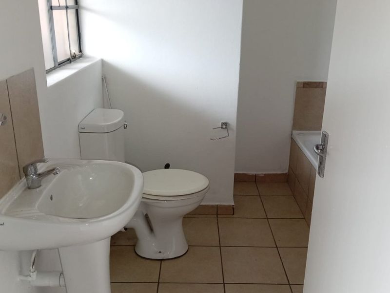 A functional bathroom featuring a pedestal basin, toilet, and bathtub with neutral tiled flooring and splashbacks.