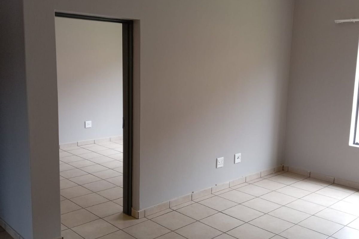 An empty living area featuring neutral grey walls and light-colored ceramic floor tiles, providing a clean and versatile space for potential residents.