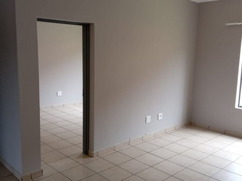 An empty living area featuring neutral grey walls and light-colored ceramic floor tiles, providing a clean and versatile space for potential residents.
