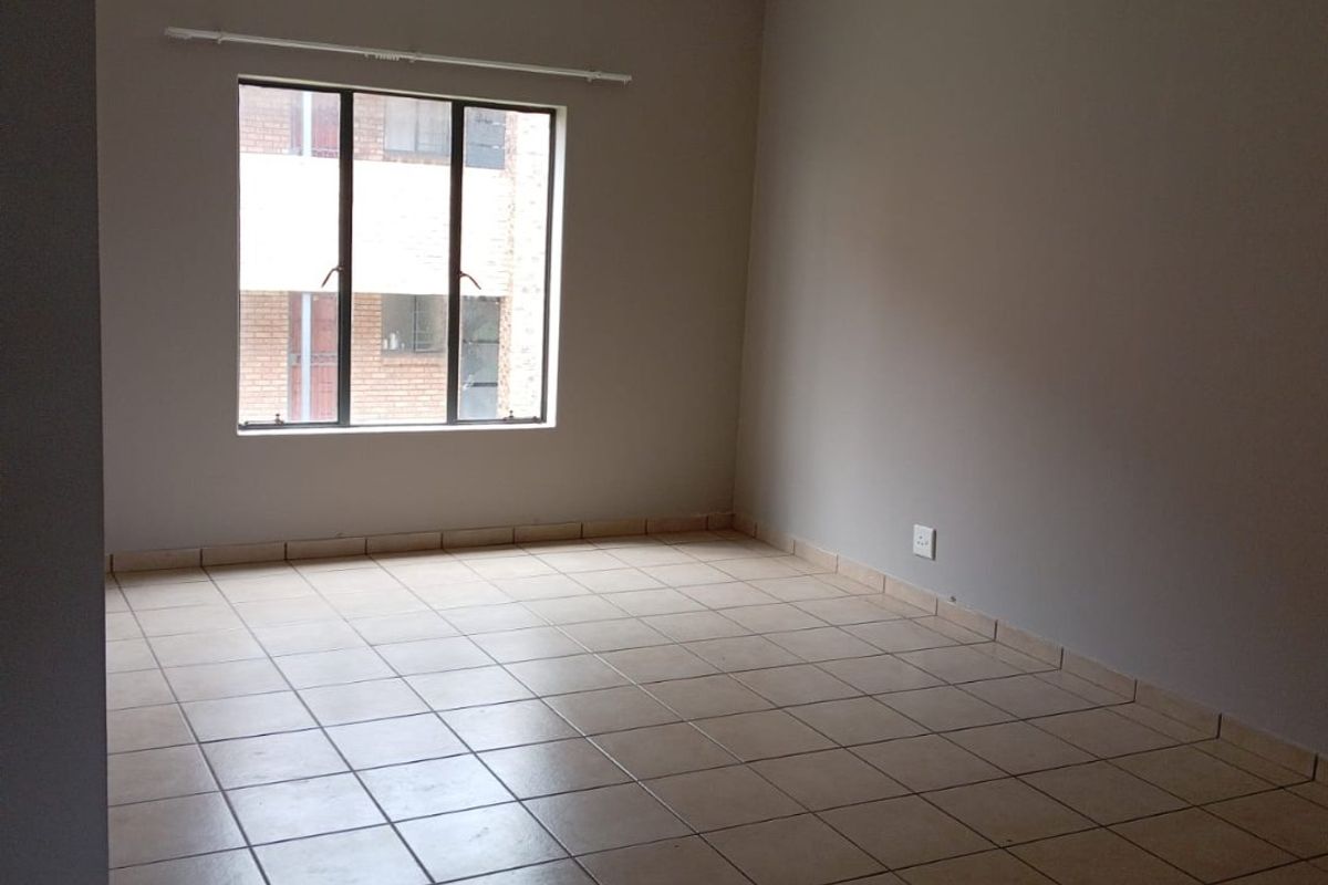 A clean, empty bedroom featuring neutral wall tones, tiled flooring, and a large window providing natural light.