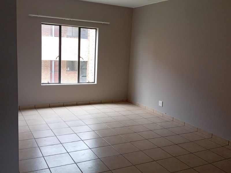 A clean, empty bedroom featuring neutral wall tones, tiled flooring, and a large window providing natural light.