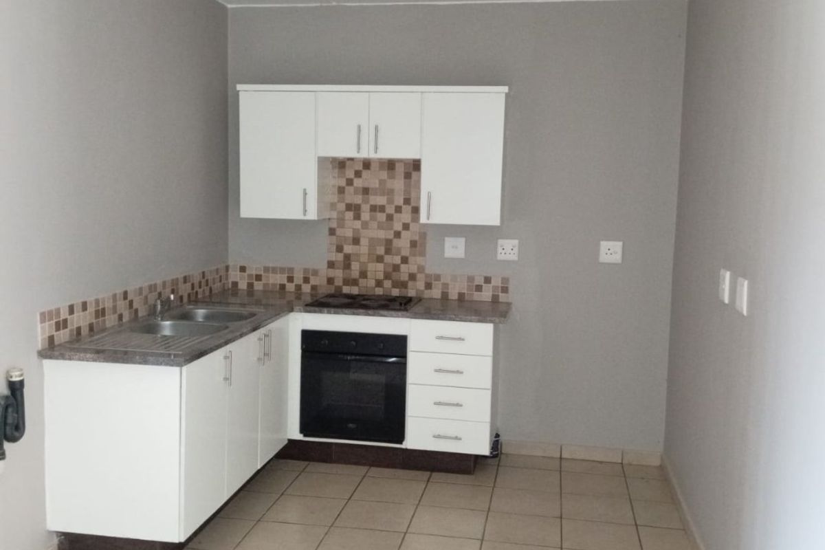 A compact, empty kitchen featuring white built-in cabinetry, a built-in oven and hob, tiled splashback, and neutral ceramic floor tiles.
