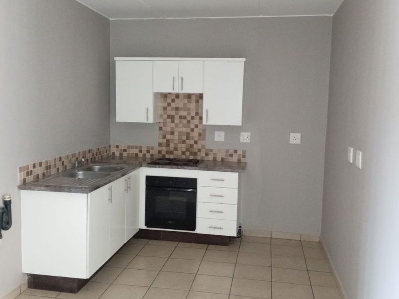 A compact, empty kitchen featuring white built-in cabinetry, a built-in oven and hob, tiled splashback, and neutral ceramic floor tiles.