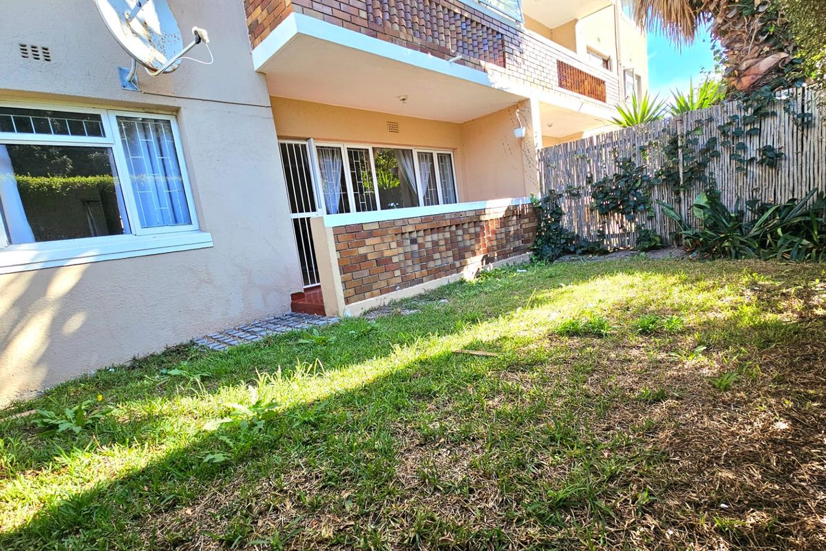 Rear exterior view of the apartment featuring a private garden area, brick facade, and security access points.