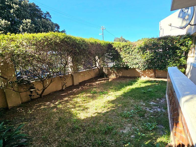 A private garden area featuring established hedging, boundary walls, and a lawn space, providing a quiet outdoor retreat for the apartment.