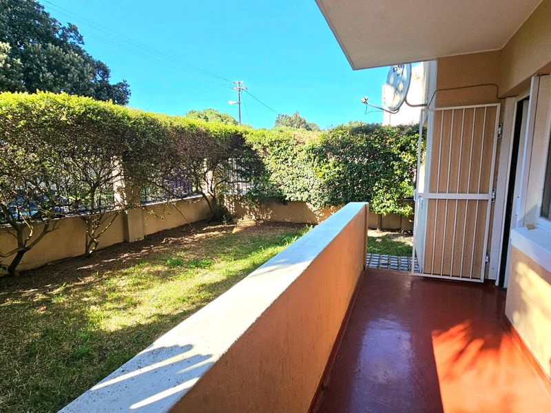 A private ground-floor balcony featuring a painted concrete floor, security gate, and direct access to a small garden area.