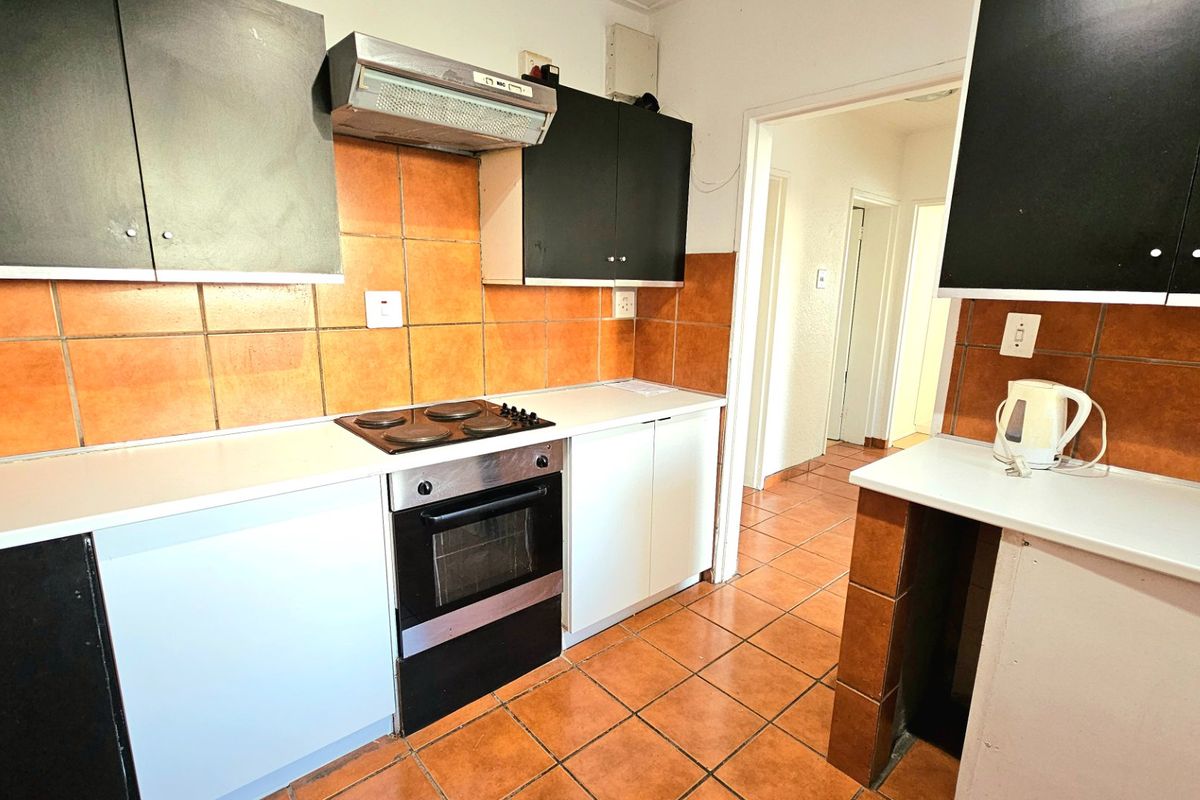 A functional kitchen featuring built-in cabinetry, an electric hob, oven, extractor fan, and tiled finishes throughout.