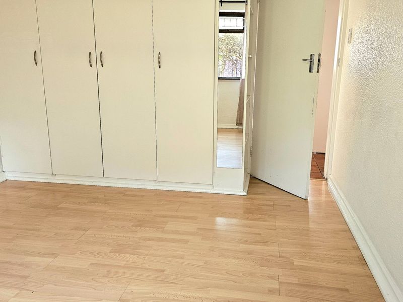 A vacant bedroom featuring light-toned laminate flooring and built-in cupboards, offering a clean, neutral canvas ready for personalization.