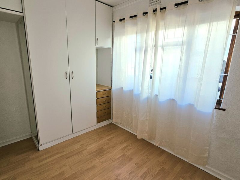 A bright, empty bedroom featuring built-in white cupboards with integrated drawers and light-toned laminate flooring.