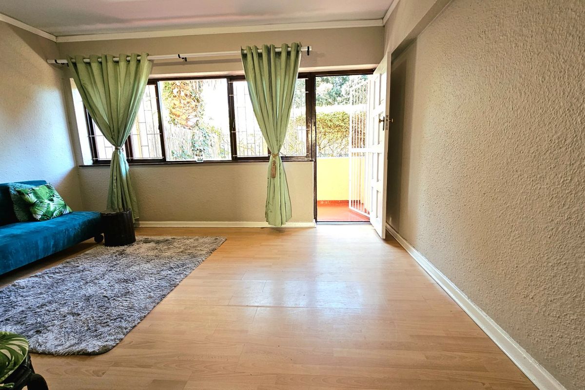A living room featuring laminate flooring, large windows with security bars, and direct access to an outdoor balcony area.