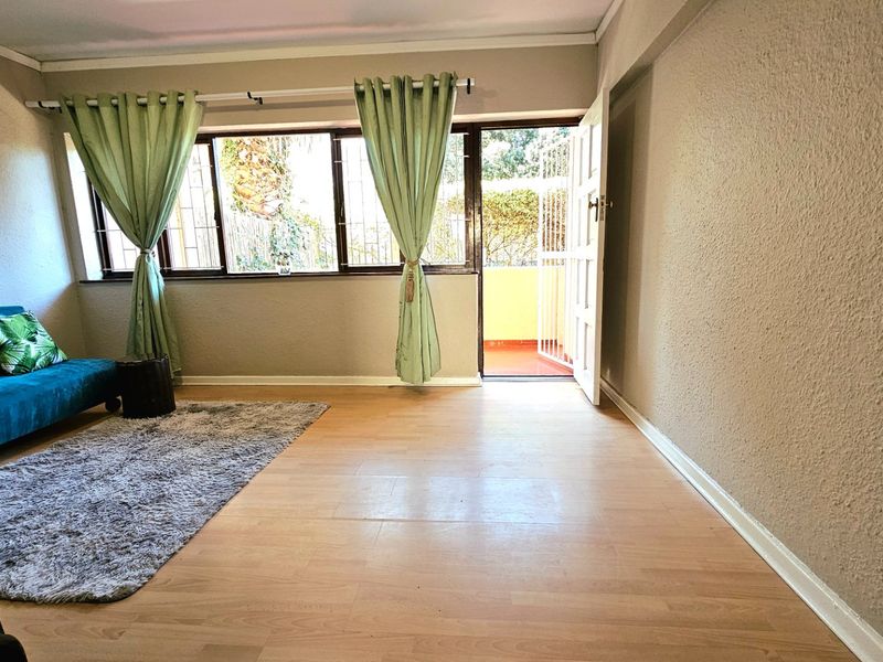A living room featuring laminate flooring, large windows with security bars, and direct access to an outdoor balcony area.