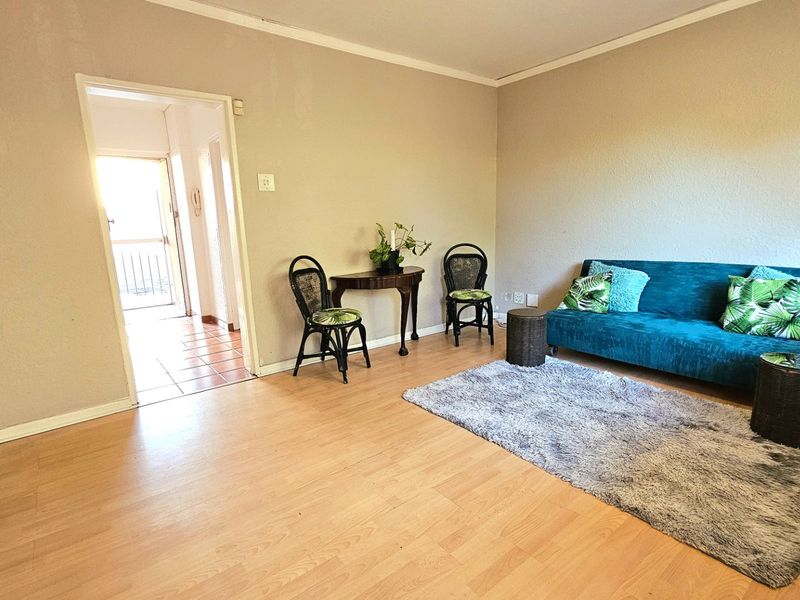 A living room featuring light-toned laminate flooring, neutral wall finishes, and coving, with an open doorway leading to an adjacent tiled hallway.
