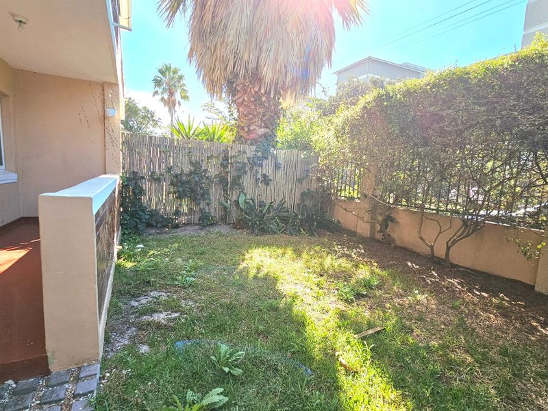 A private rear garden area featuring a small patio, boundary wall, and lawn, offering potential for outdoor landscaping and improvement.