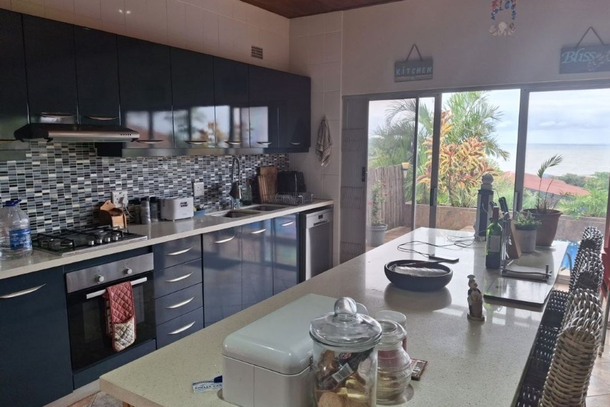 Modern kitchen featuring dark cabinetry, stone countertops, a central island, built-in oven, gas hob, and sliding glass doors leading to an outdoor patio area.