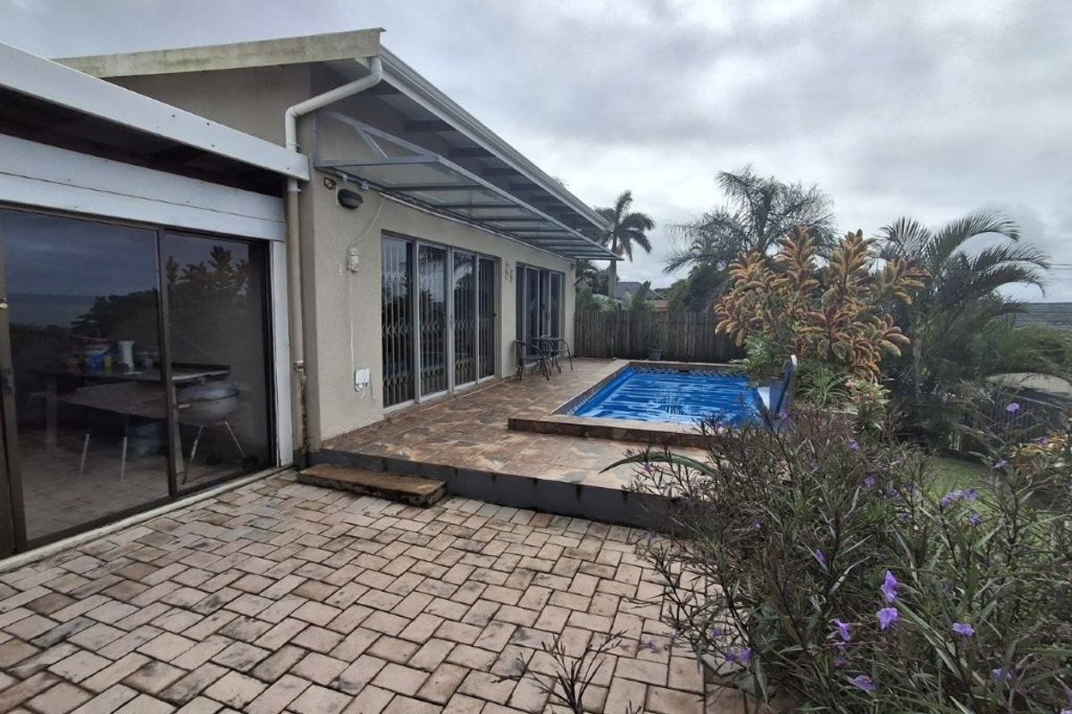Rear exterior view featuring a paved patio area, a built-in swimming pool, and sliding glass doors providing access to the home's interior.