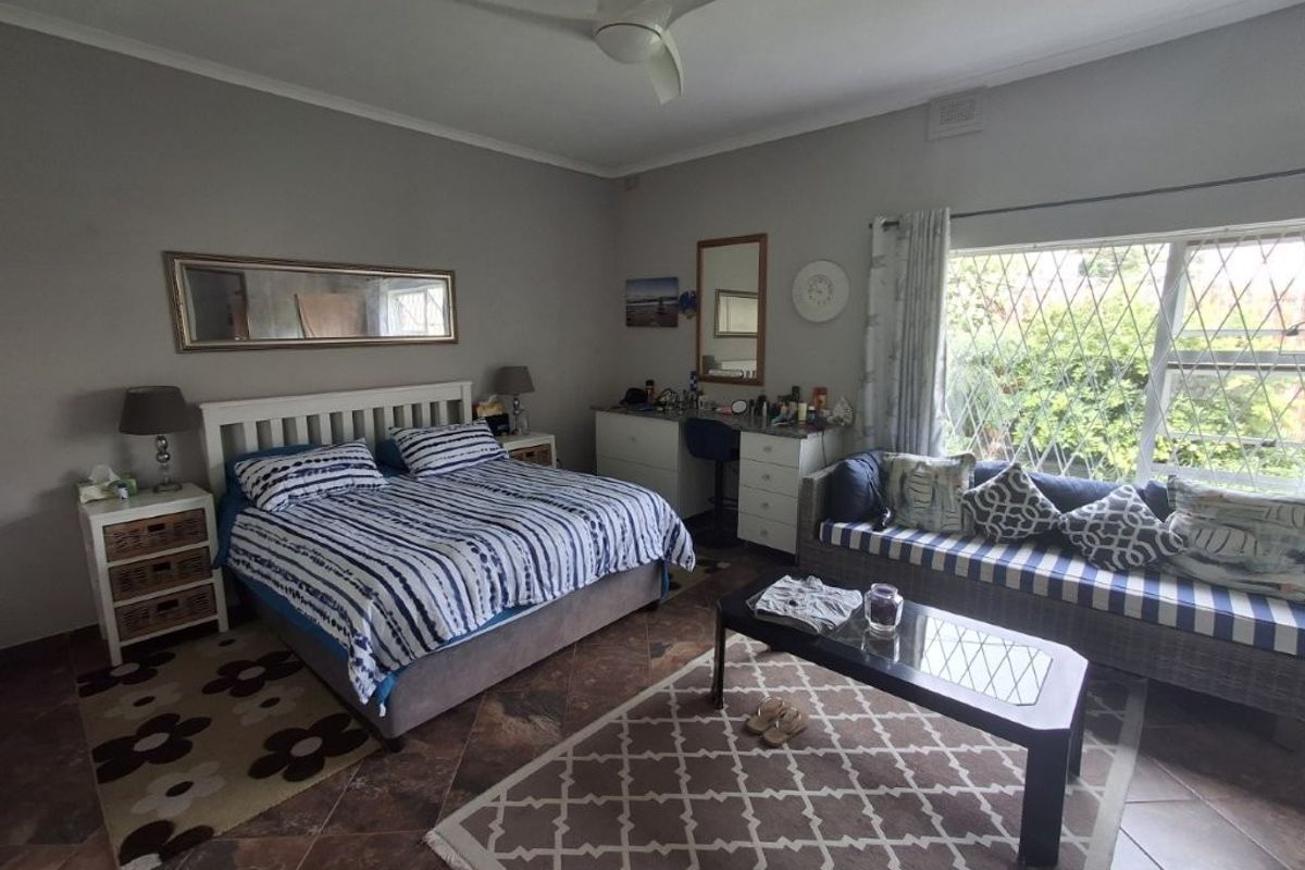 Spacious bedroom featuring tiled flooring, a ceiling fan, and large windows with security bars, offering a comfortable and functional living space.