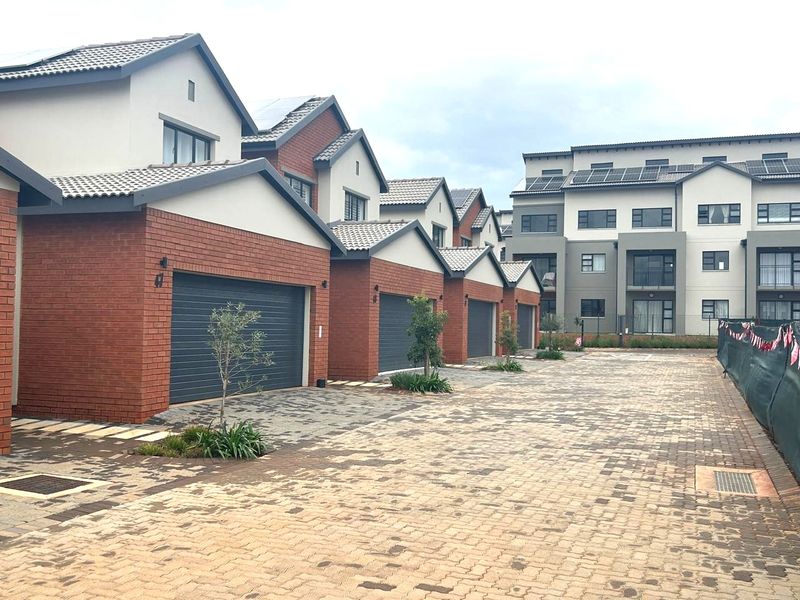 A modern apartment complex featuring a row of brick-faced garages with paved driveway access and solar panel installations on the roof.