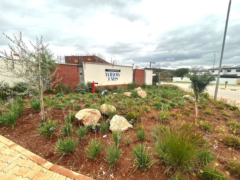 The entrance to Willow Falls estate featuring a brick boundary wall, landscaped garden beds with decorative rocks, and a paved walkway.