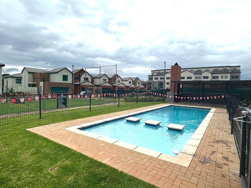 Communal swimming pool area featuring paved surround, pergola, and adjacent lawn within a residential apartment complex.