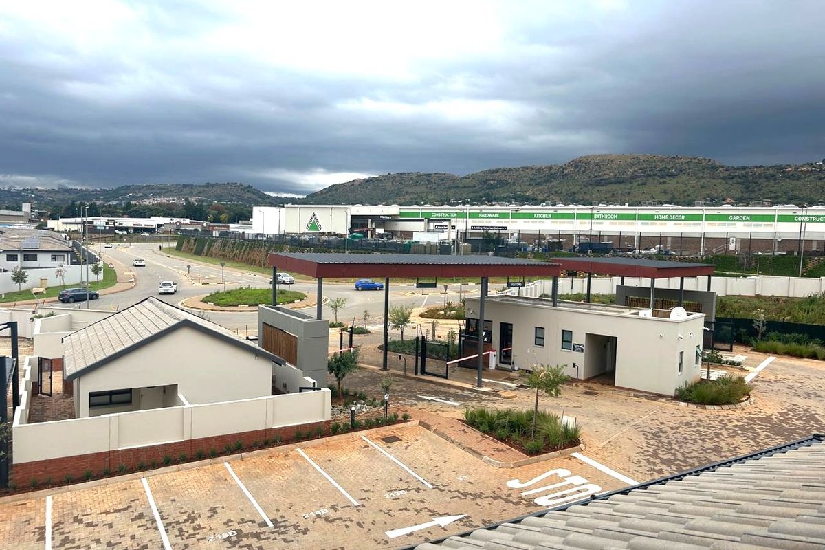 An elevated view of the apartment complex entrance, featuring a security gatehouse, paved parking bays, and surrounding infrastructure.
