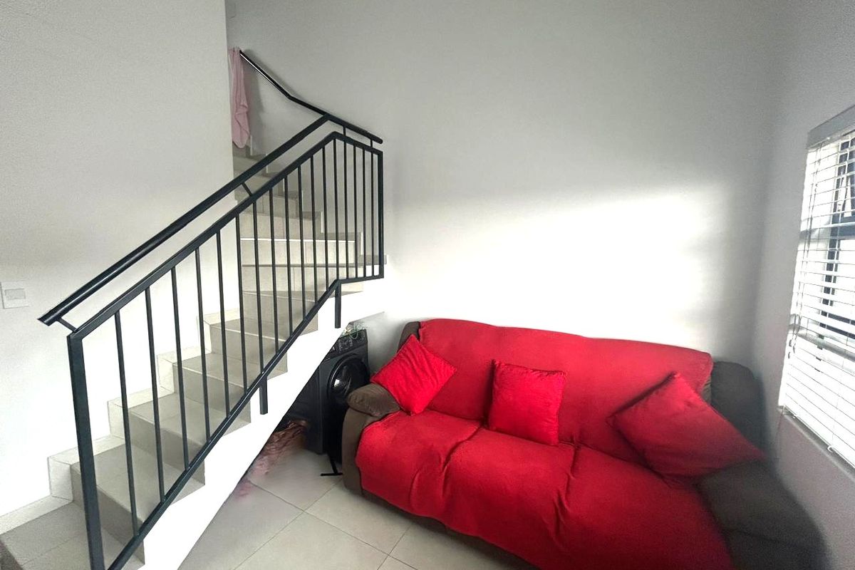 Living area featuring tiled flooring, a staircase with a black metal balustrade, and natural light through venetian blinds.