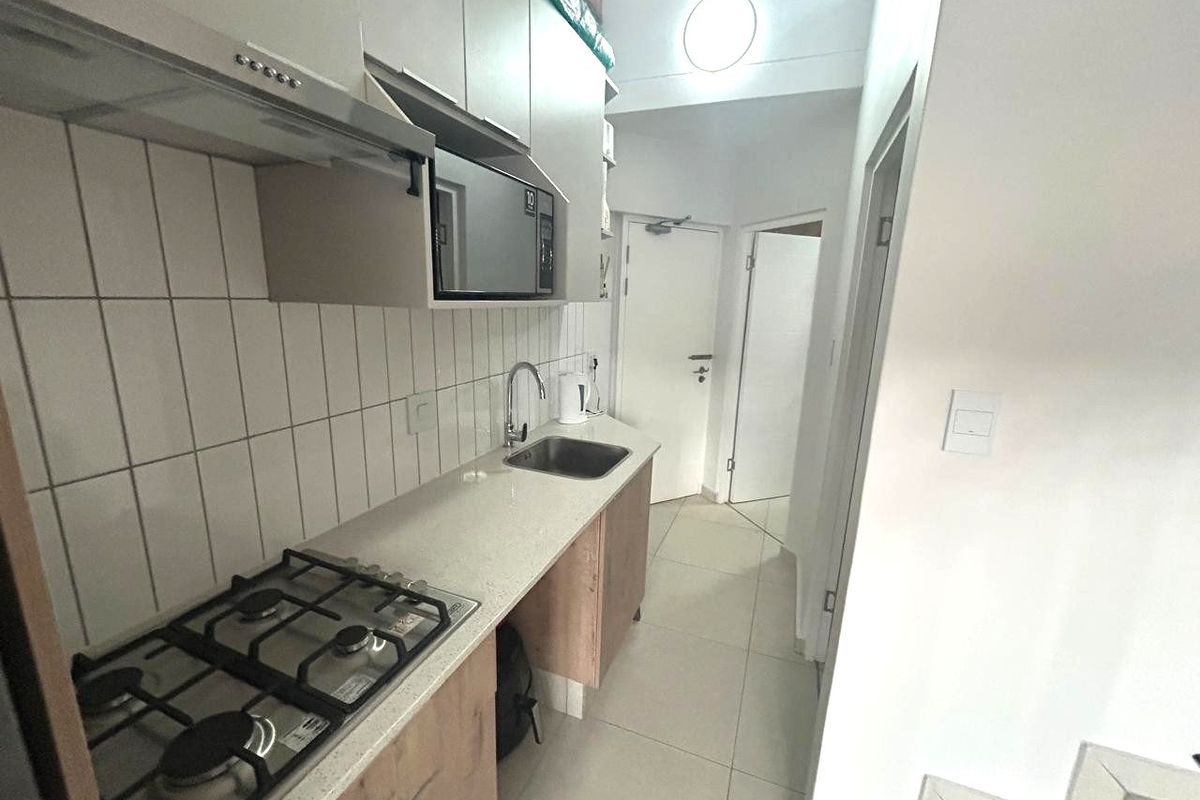 A compact, modern kitchen featuring a gas hob, extractor fan, built-in microwave, stone countertops, and tiled backsplash with neutral cabinetry.