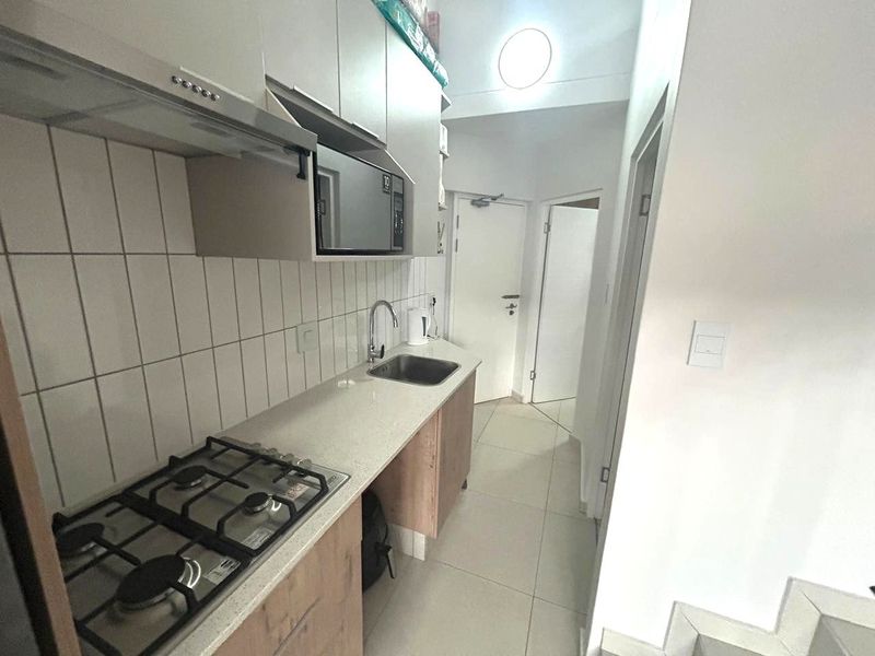 A compact, modern kitchen featuring a gas hob, extractor fan, built-in microwave, stone countertops, and tiled backsplash with neutral cabinetry.
