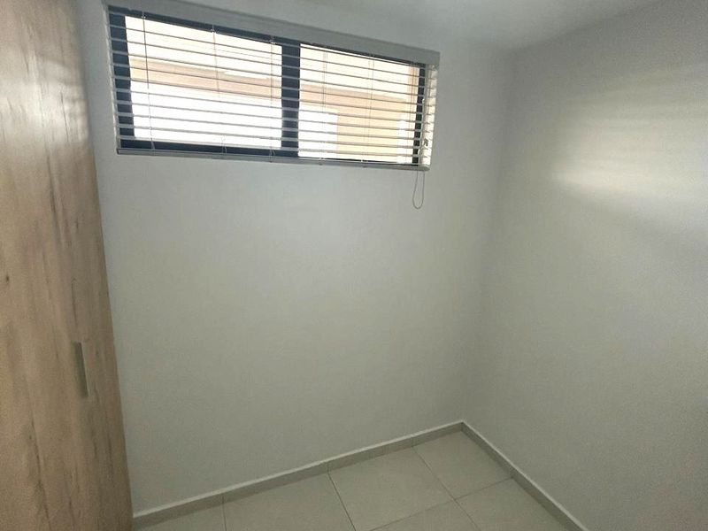 A clean, empty bedroom featuring neutral tiled flooring, a built-in wardrobe, and a window fitted with venetian blinds.
