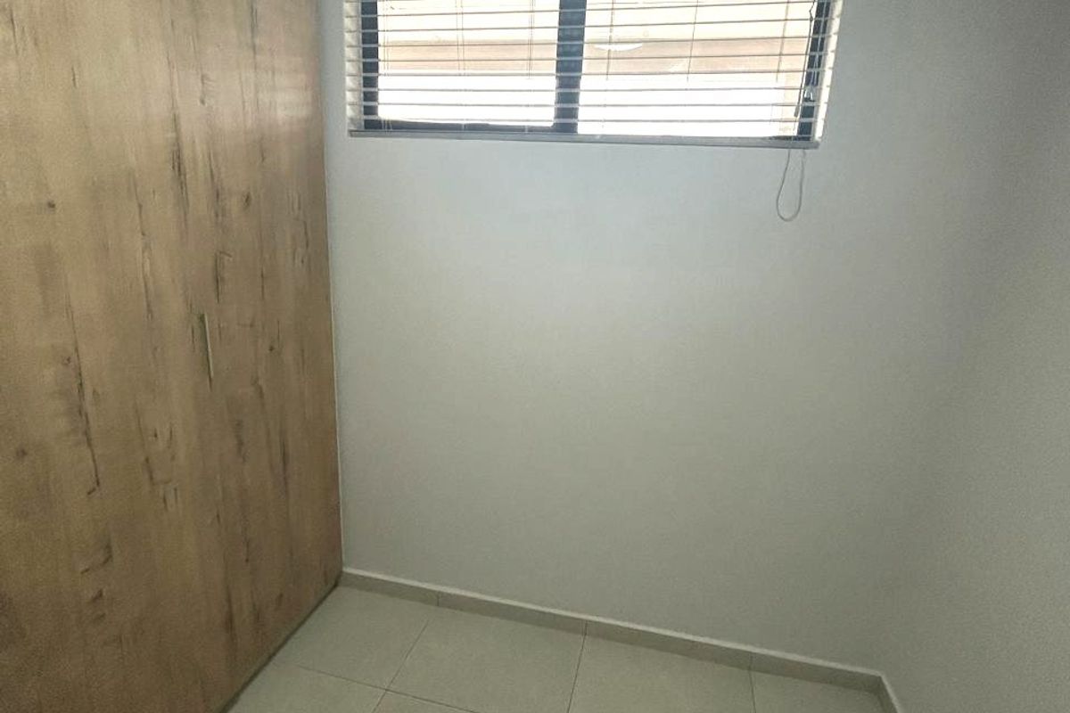 A clean, empty bedroom featuring neutral tiled flooring, a large built-in wooden wardrobe, and a window fitted with venetian blinds.