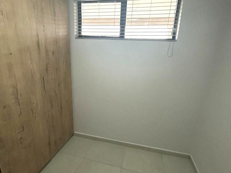 A clean, empty bedroom featuring neutral tiled flooring, a large built-in wooden wardrobe, and a window fitted with venetian blinds.